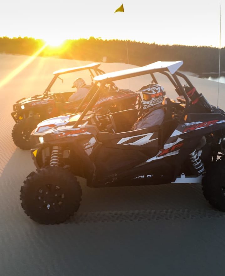Two guests sitting in RZRs at sunset