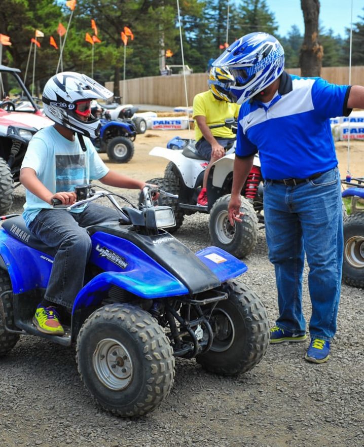 Adult talking to a child on an ATV, both wearing helmets.