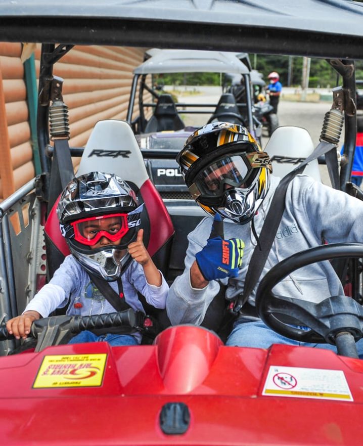 Child and guest sitting in an ATV giving the thumbs up